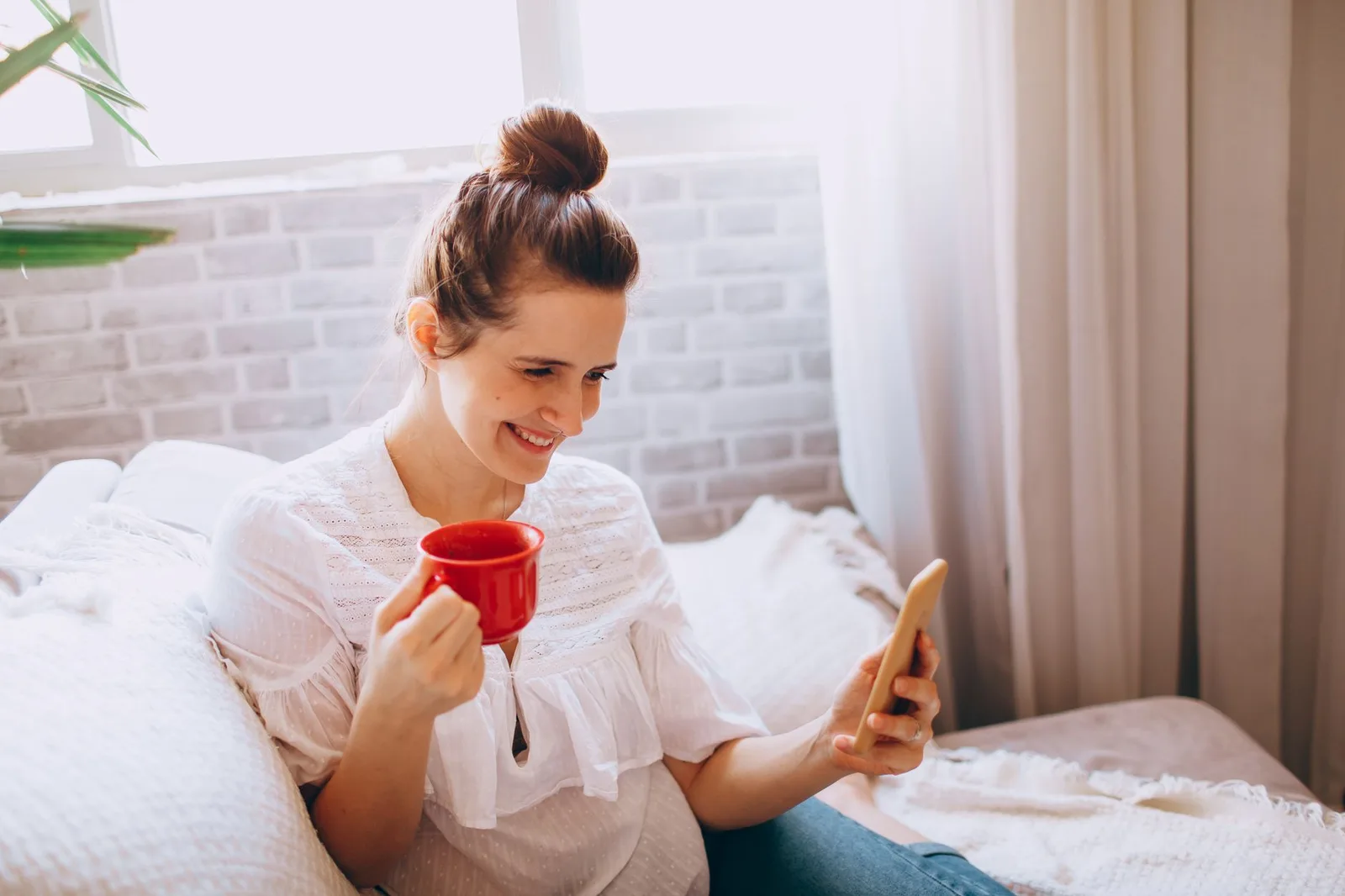Buổi sáng bên cửa sổ, cô gái trẻ cầm điện thoại bên tách cà phê