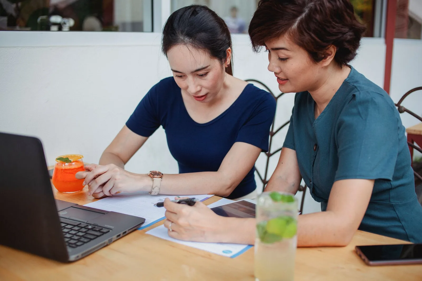 Nhóm bạn châu Á trò chuyện quanh laptop ở quán